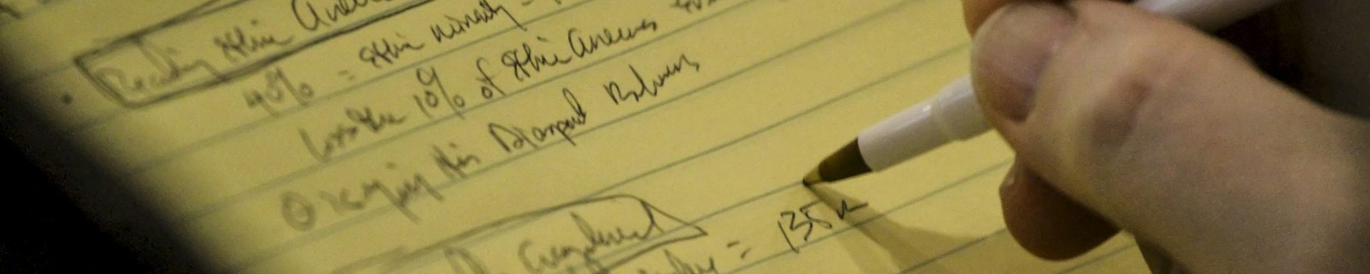 Hand, die handschriftliche Notizen auf einen gelben Notizblock schreibt