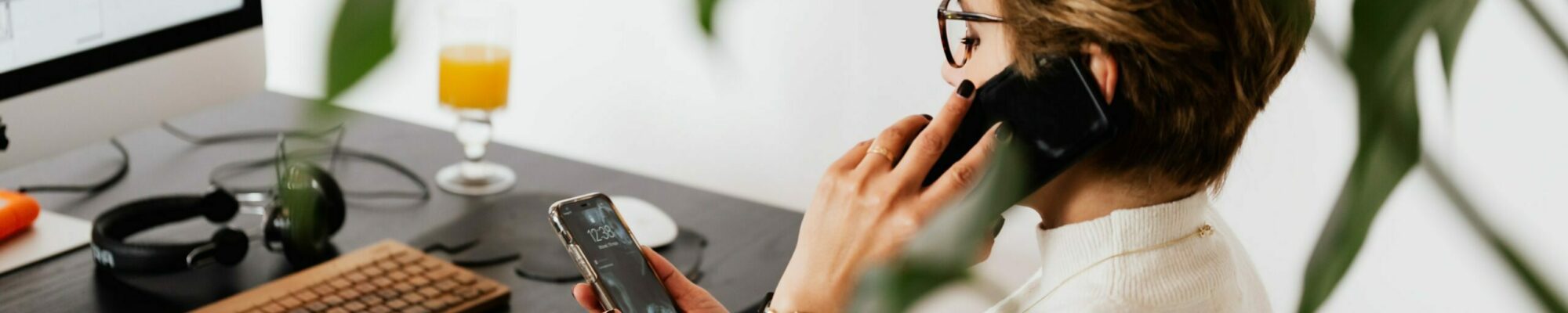 Frau am Schreibtisch, die gleichzeitig mit zwei Mobiltelefonen hantiert